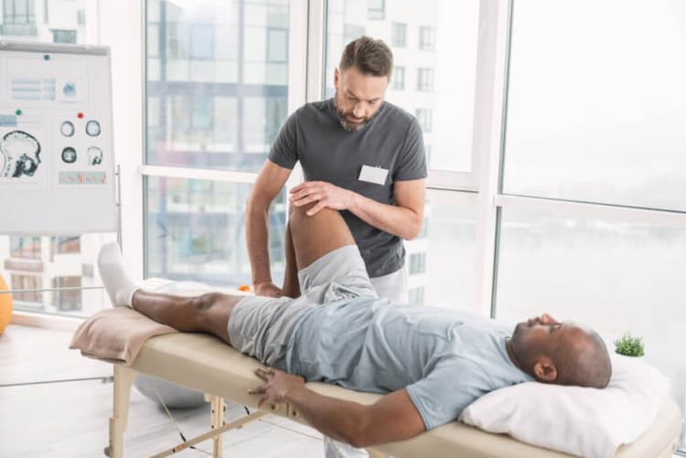 man lying on physical therapy table with therapist moving his lower leg