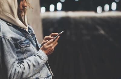 Girl pointing finger on screen smartphone on background illumination bokeh color light in night atmospheric city bridge hipster using in female hands and texting mobile phone mockup glitter street lifestyle
