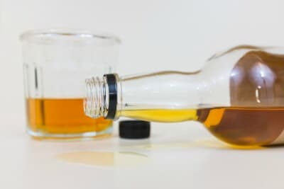 close up image of opened alcohol bottled that spilled on white counter and a glass of half drunk alcohol
