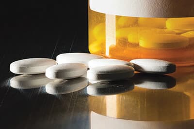 Prescription bottle with blank label for copy space and white pills or tablets on metal table for opioid epidemic illustration